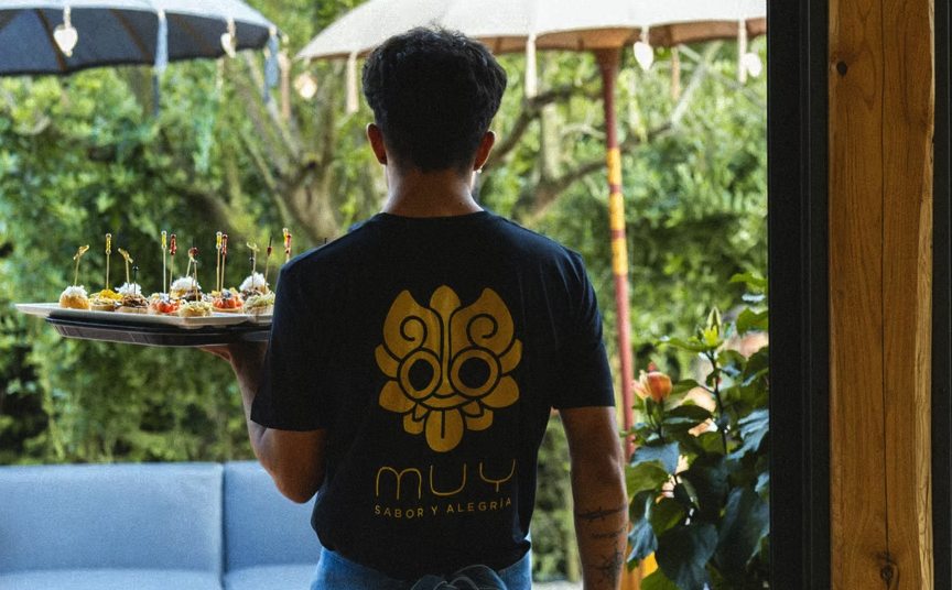 Un cameriere con la maglietta MUY porta un vassoio di finger food in giardino