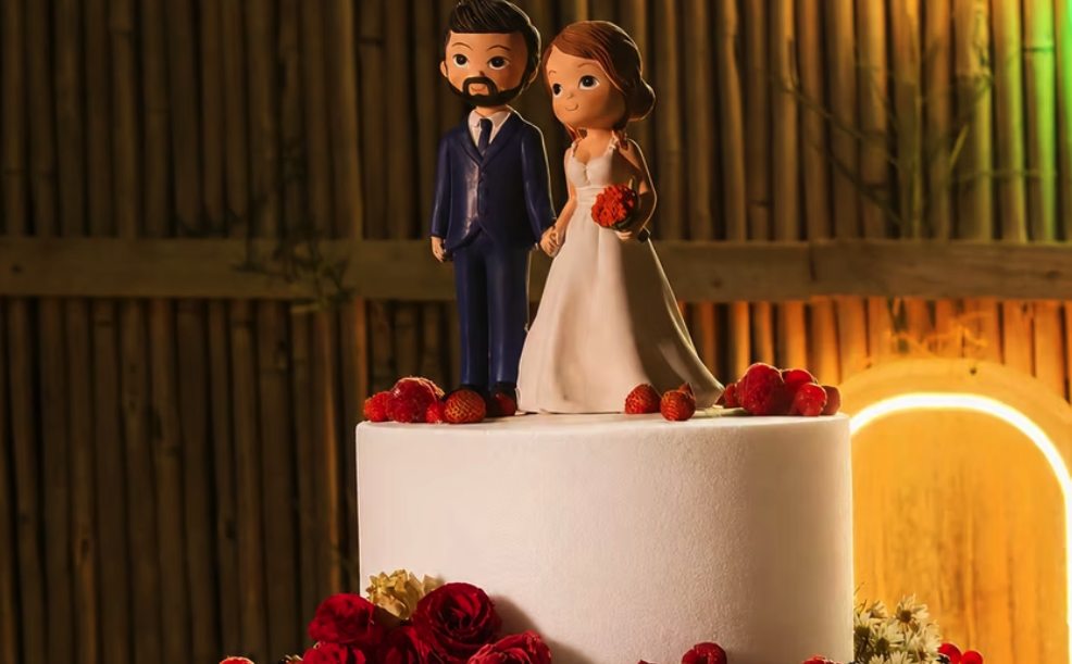 Torta nuziale bianca a due piani con rose rosse e le statuine degli sposi
