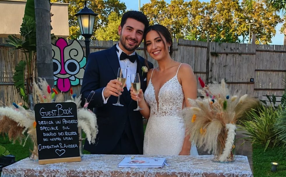 Gli sposi brindano davanti al tavolo del guest book in giardino