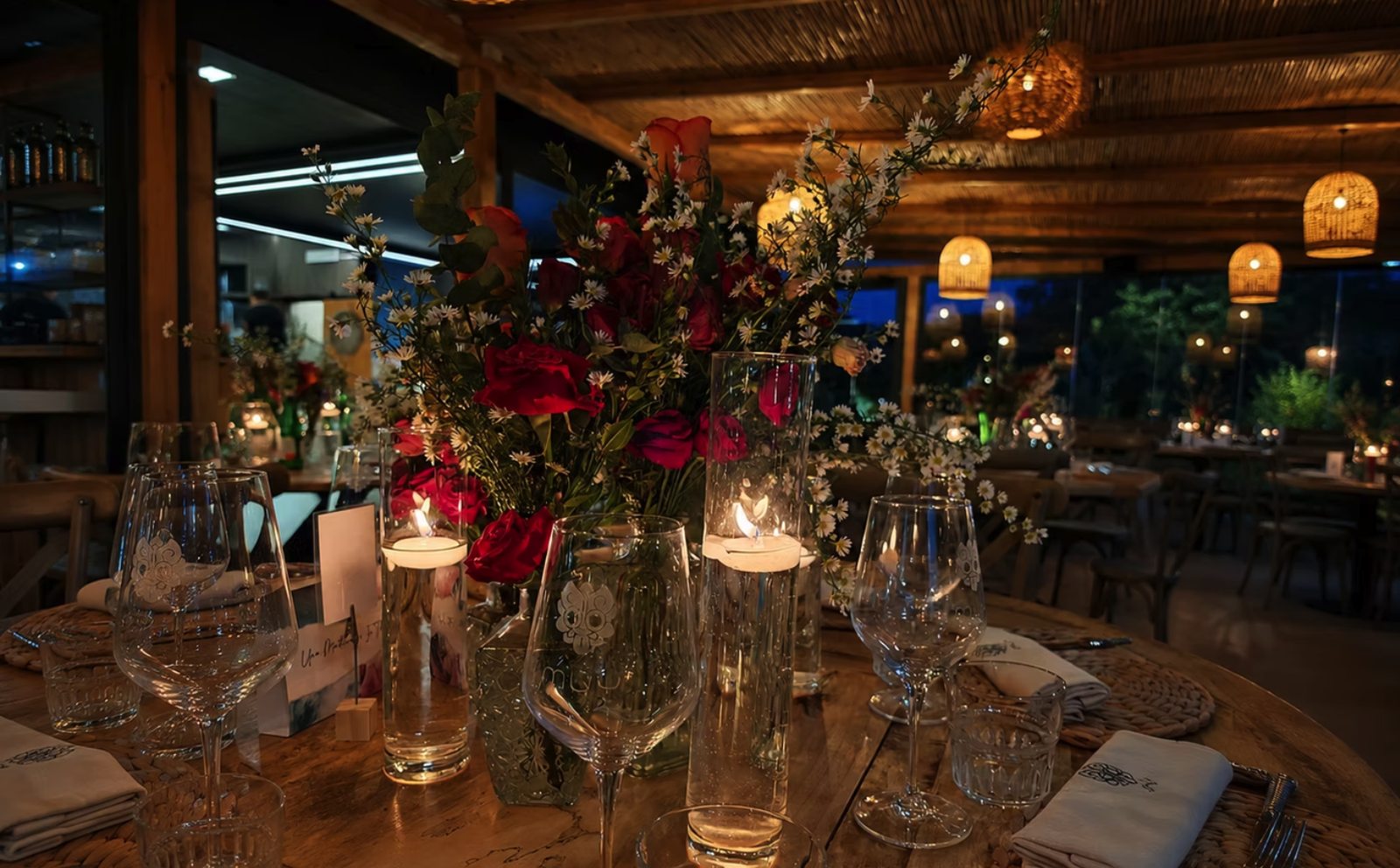 Tavola apparecchiata con rose rosse, candele e calici con il logo MUY
